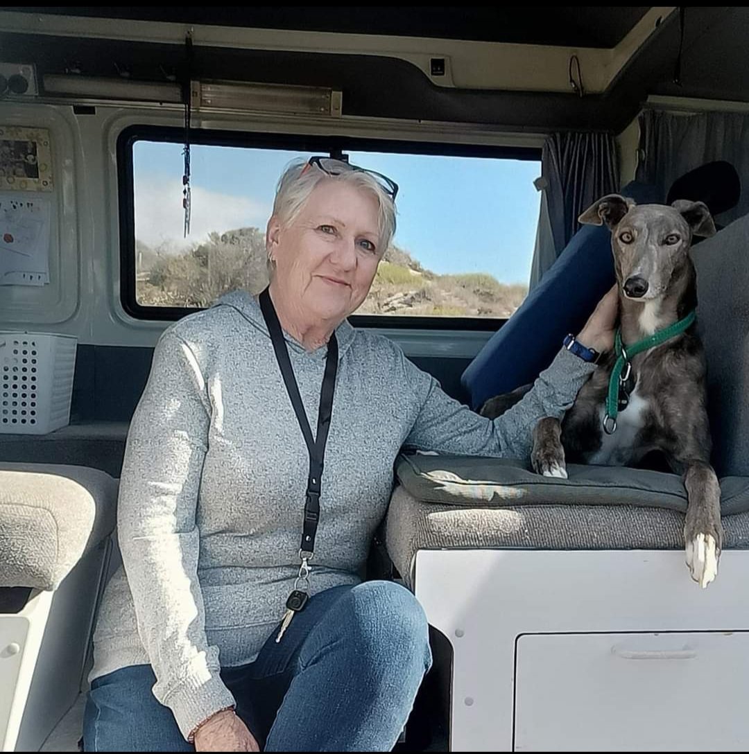 Colleen Moyne sitting in the back of her campervan beside Winter, her grey greyhound, with scrubland visible through the window behind them.